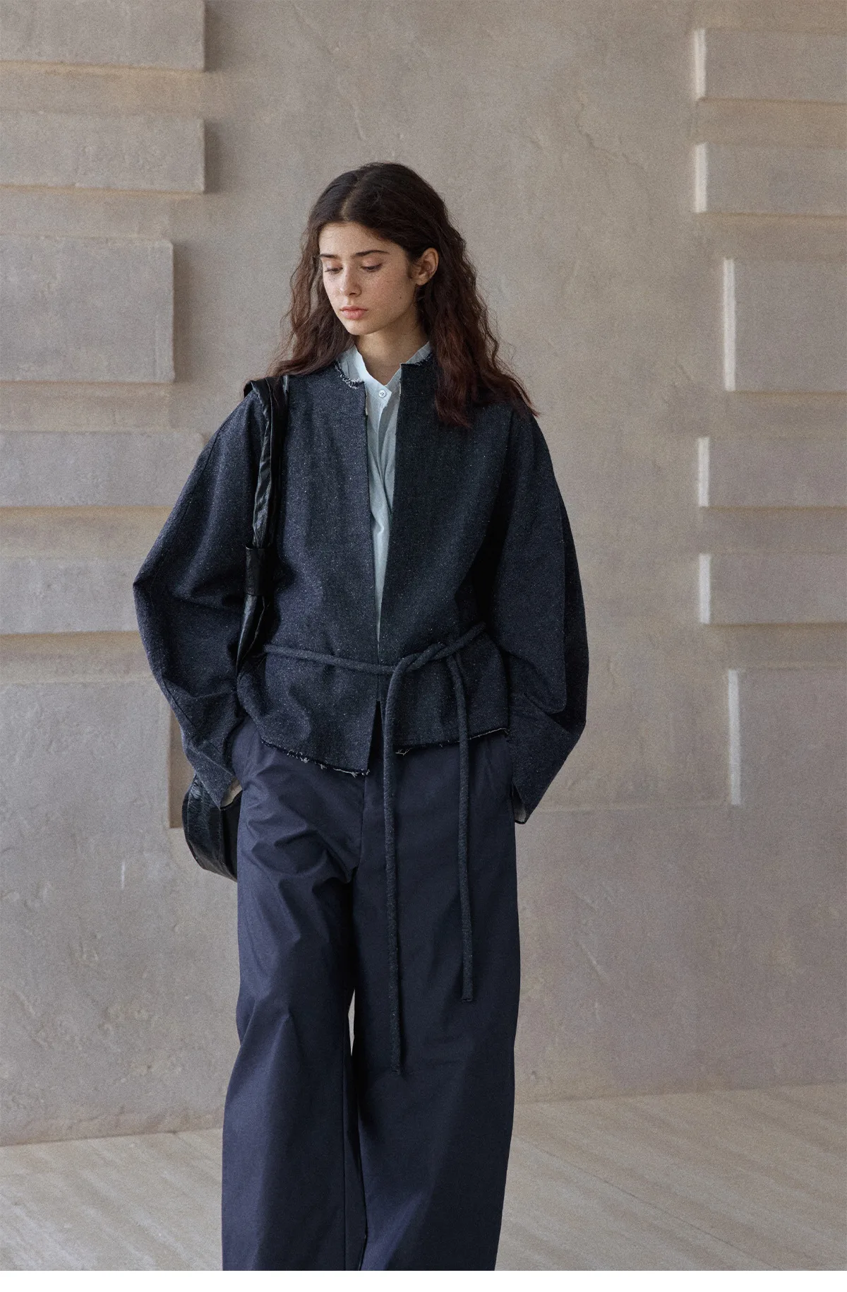Woman wearing a dark cotton-linen cropped jacket with waist tie and raw edges